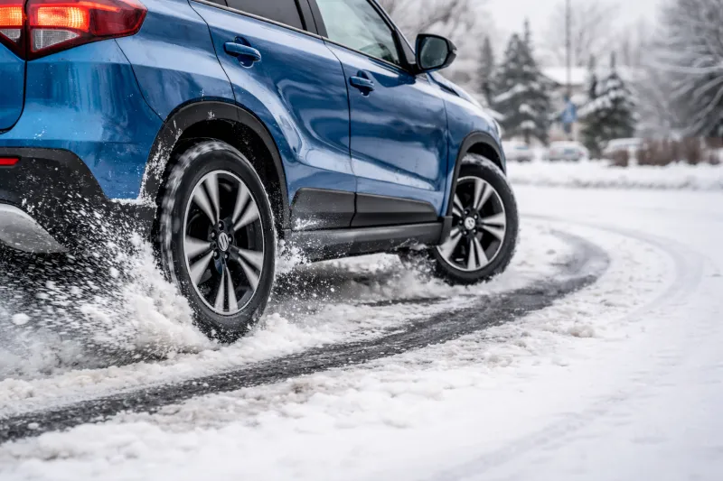 Suzuki Vitara з системою ALLGRIP повертає на засніженій дорозі в передмісті, фокус на колеса та зчеплення